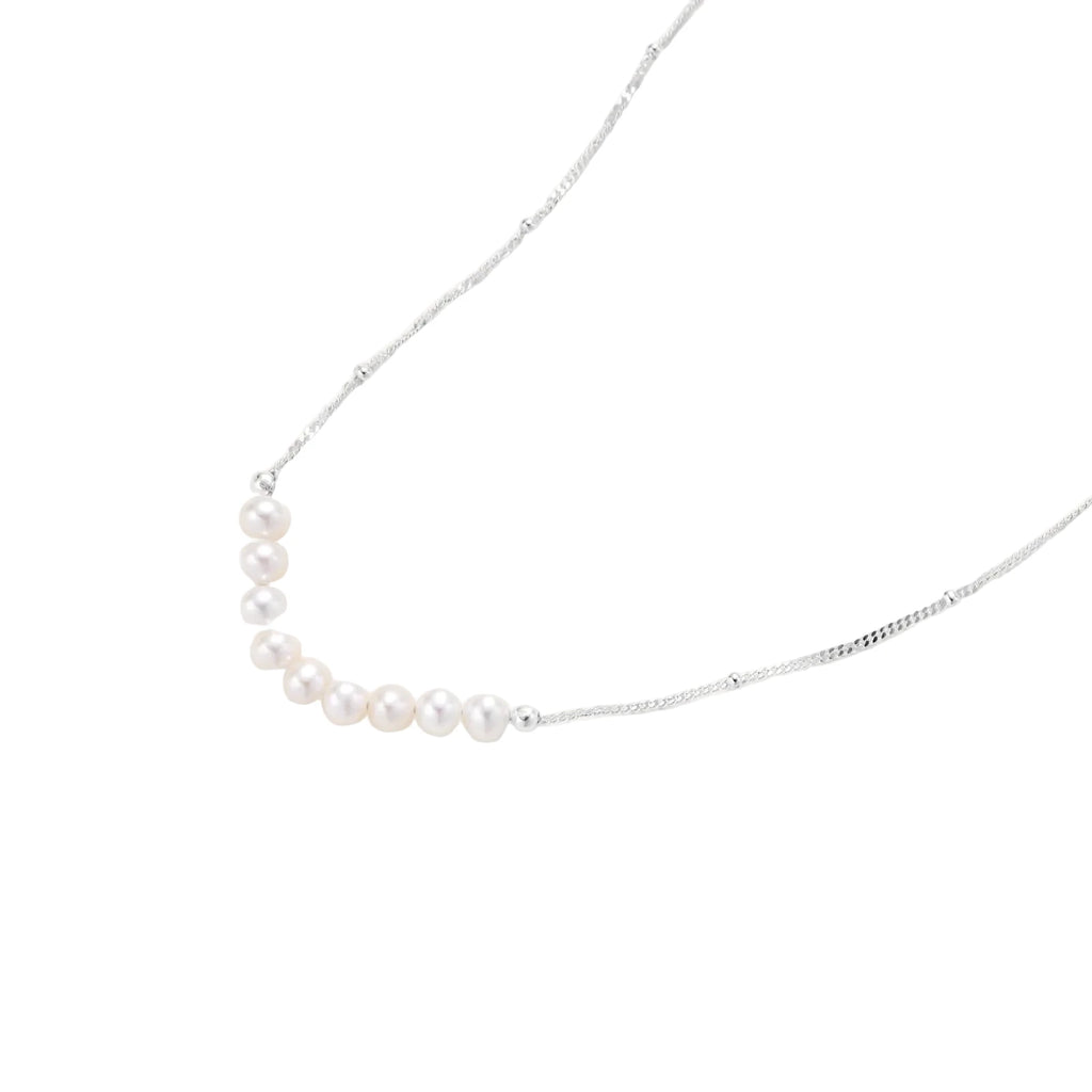 Delicate sterling silver chain necklace with small freshwater pearls arranged in a curved smile arc on cream background.