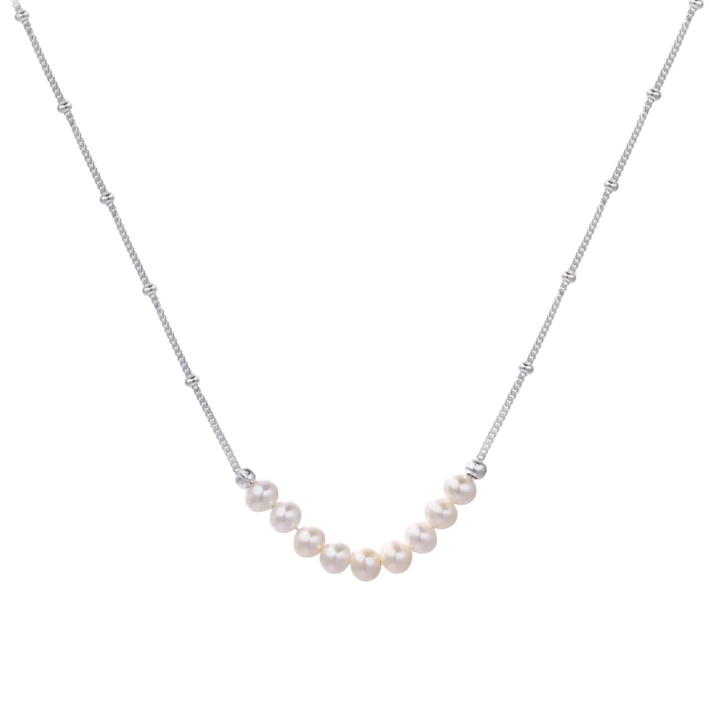 Delicate sterling silver chain necklace with small freshwater pearls arranged in a curved smile arc on cream background.