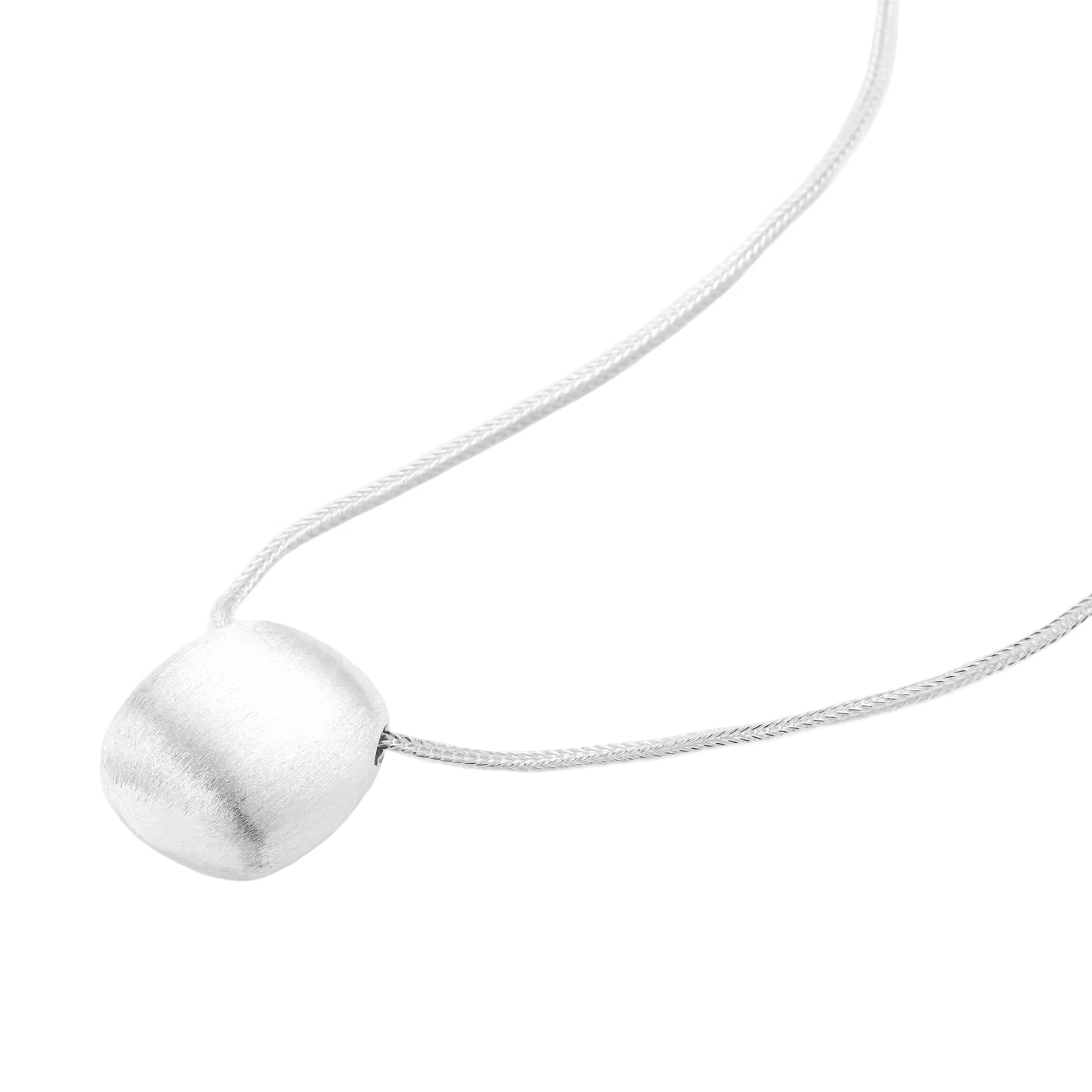 Minimalist brushed sterling silver dome pendant on delicate chain against cream background, showing matte textured finish